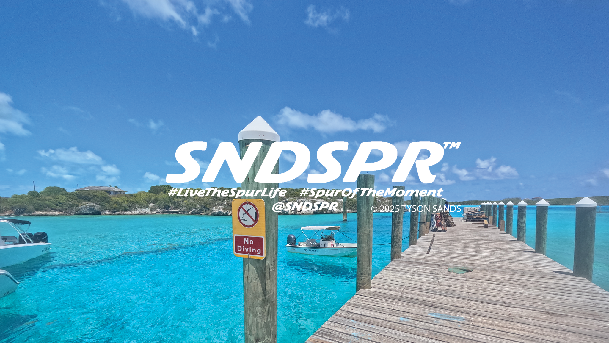 SNDSPR logo over turquoise water and a wooden dock. Banner reads: Live the Spur Life, Spur of the Moment, @SNDSPR. Photograph credited to Tyson Sands, 2025.